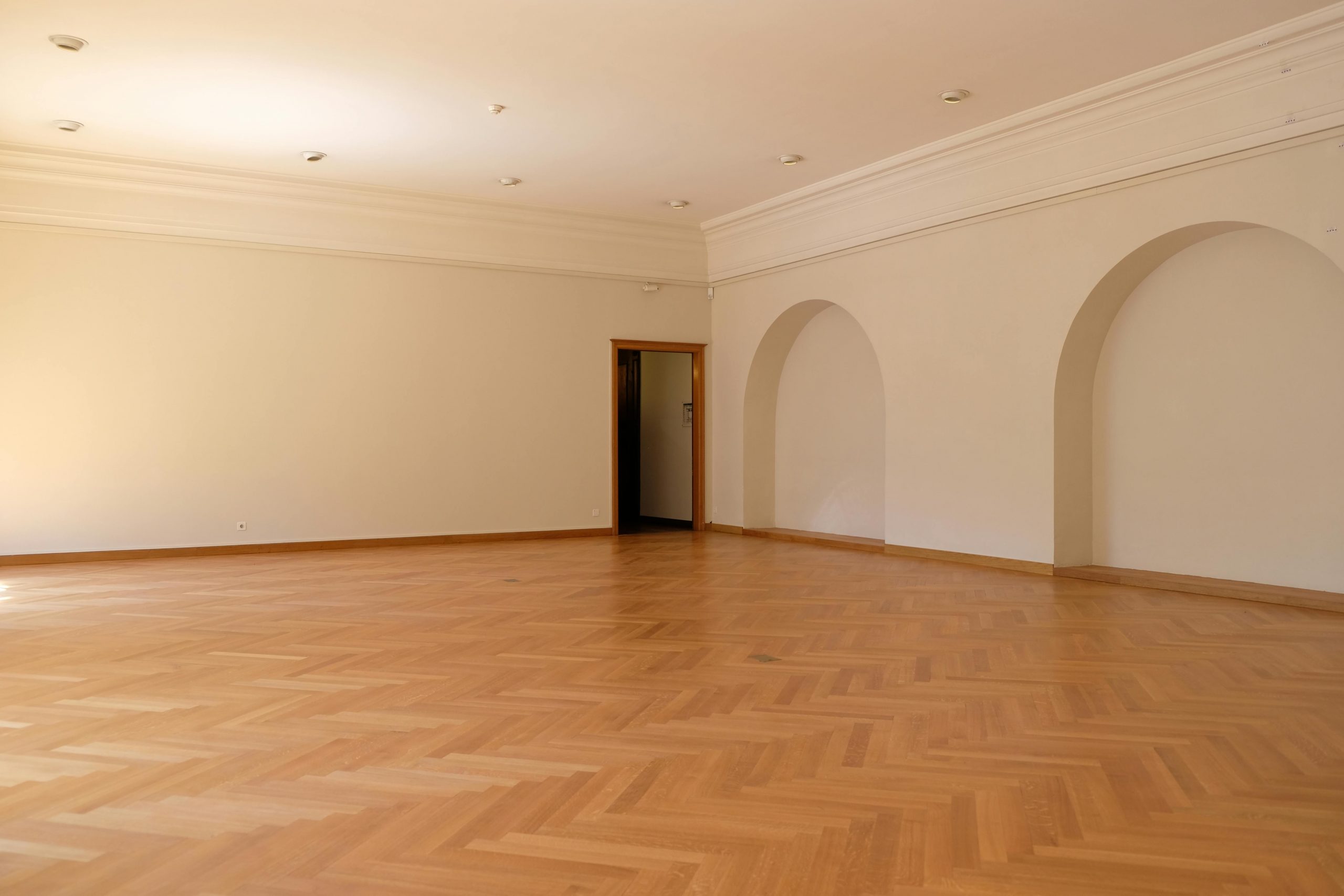 A large empty room with elegant wooden flooring, arches, and natural lighting, perfect for interior design inspiration.